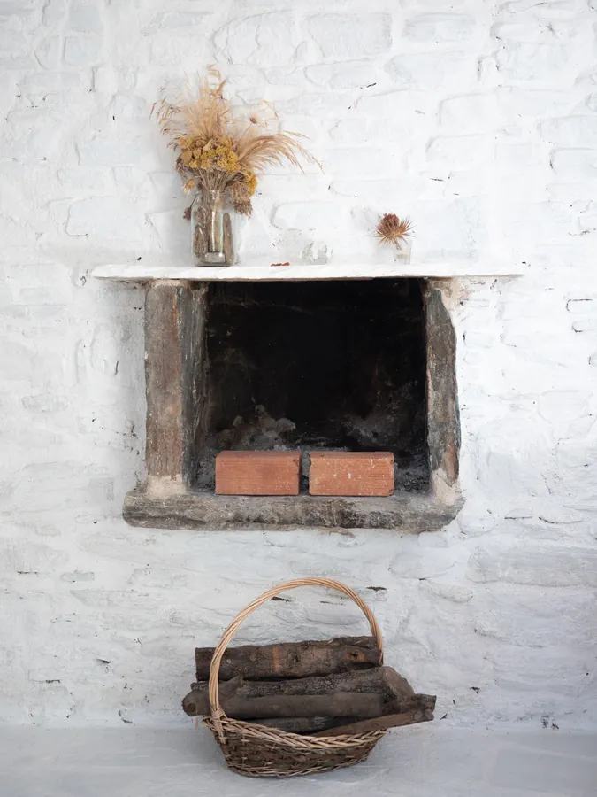 A fireplace in a whitewashed wall, a basket of firewood beneath